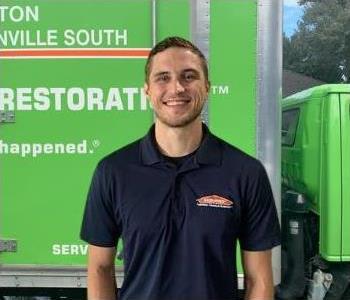 male employee with brown hair and a black shirt in front of a green SERVPRO truck