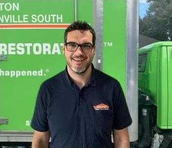 male employee with brown hair and a black shirt in front of a green SERVPRO truck
