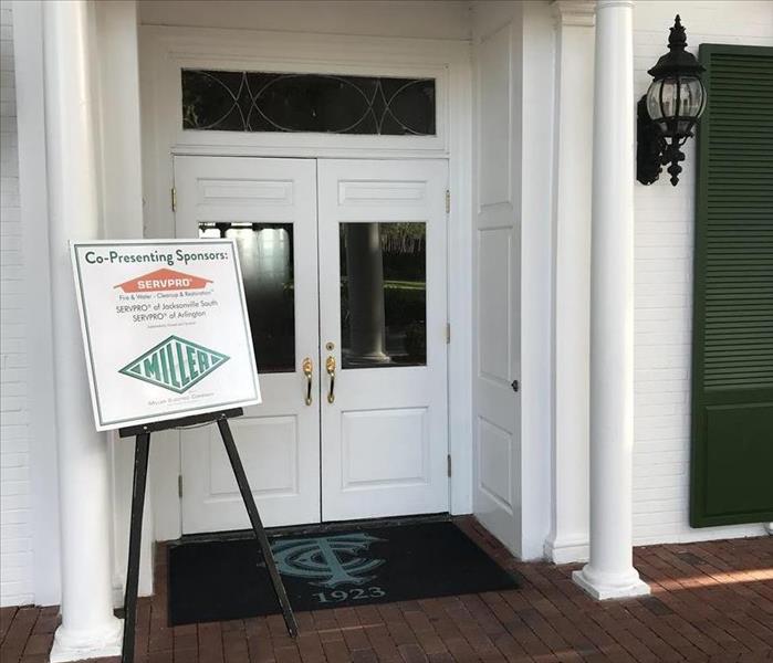 A front door with a sign propped up in front of the door with the words SERVPRO on it.  